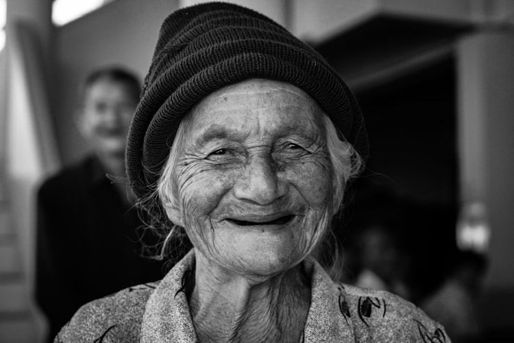 old woman with hearing aids wears black hat and smiles