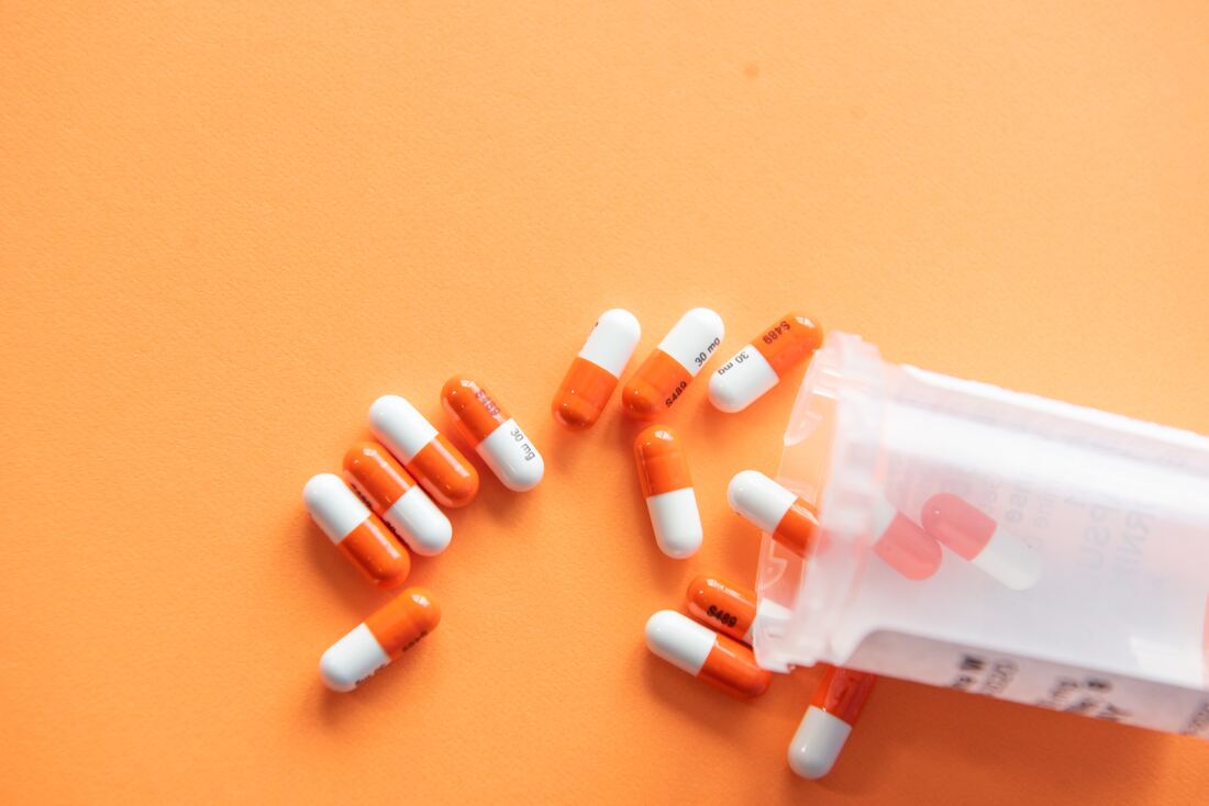 orange and white blood pressure pills that cause tinnitus spill out from medicine bottle onto orange backdrop