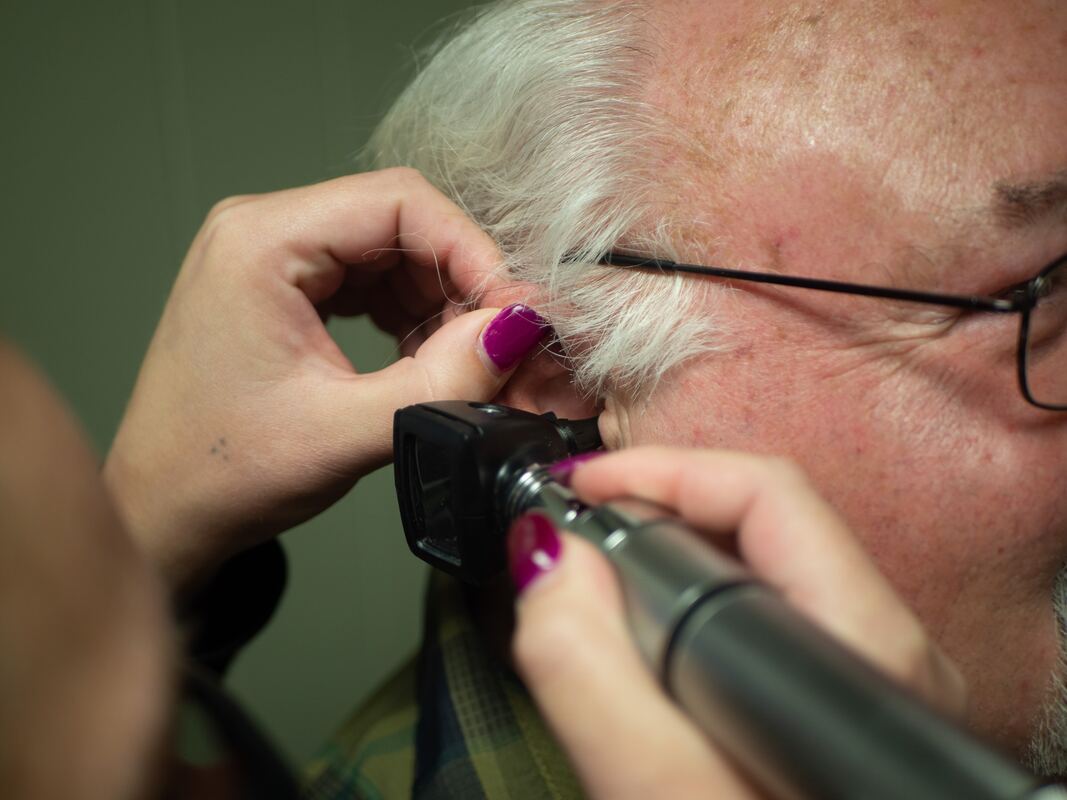 A hearing healthcare provider uses an otoscope to check a man's ear during a hearing appointment.