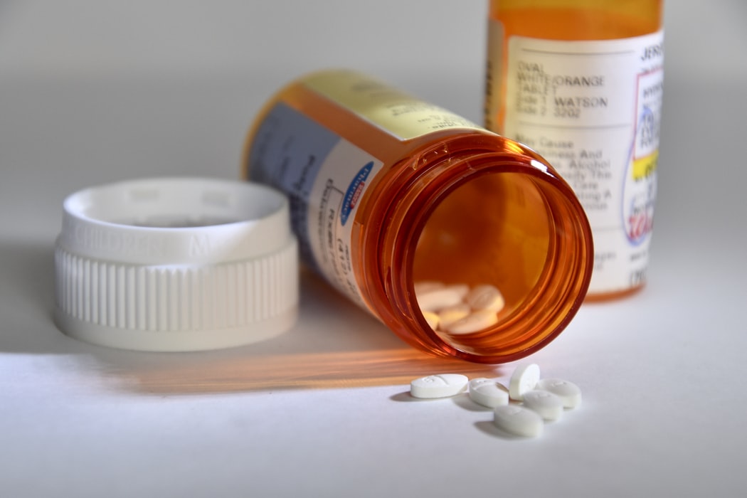 An orange prescription bottle with white pills spills onto a white surface while another bottle stands upright.