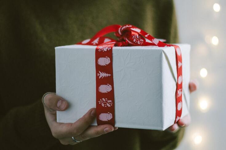 A woman in a green sweater holds hearing aids gift-wrapped in white paper and a red and white bow.