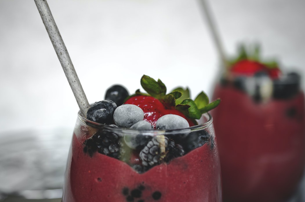 red smoothie with blueberries strawberries and blackberries in a glass with a straw
