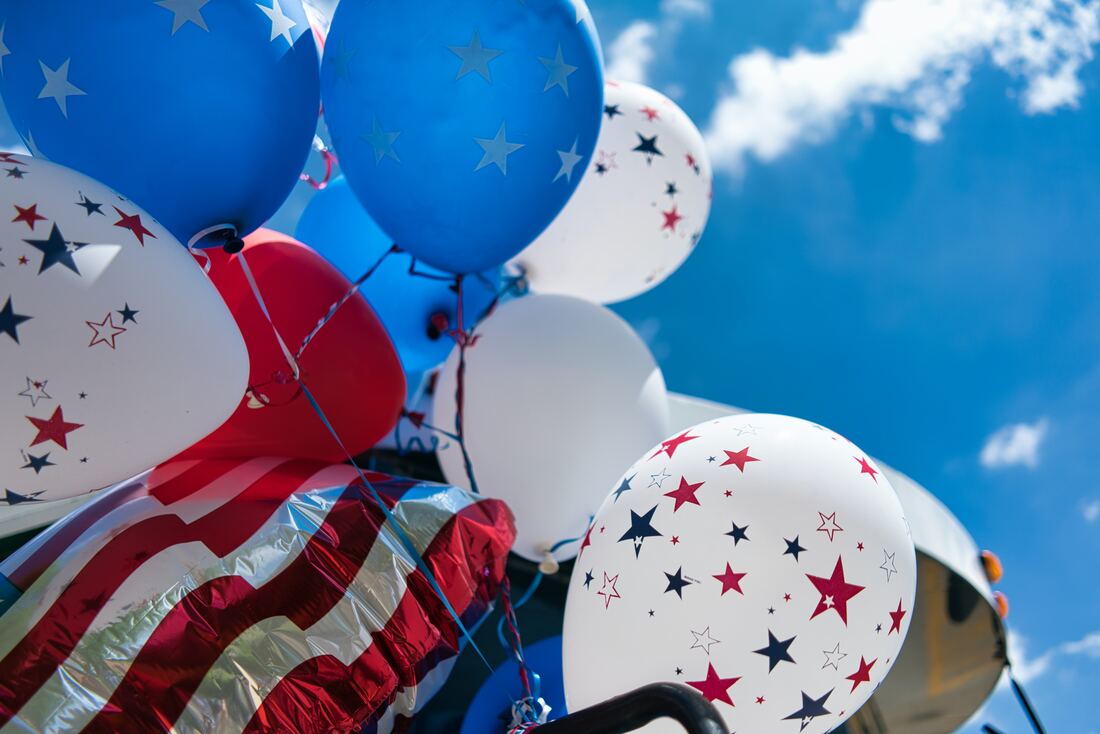 decorations for the fourth of july with red white and blue balloons beneath a blue sky with clouds