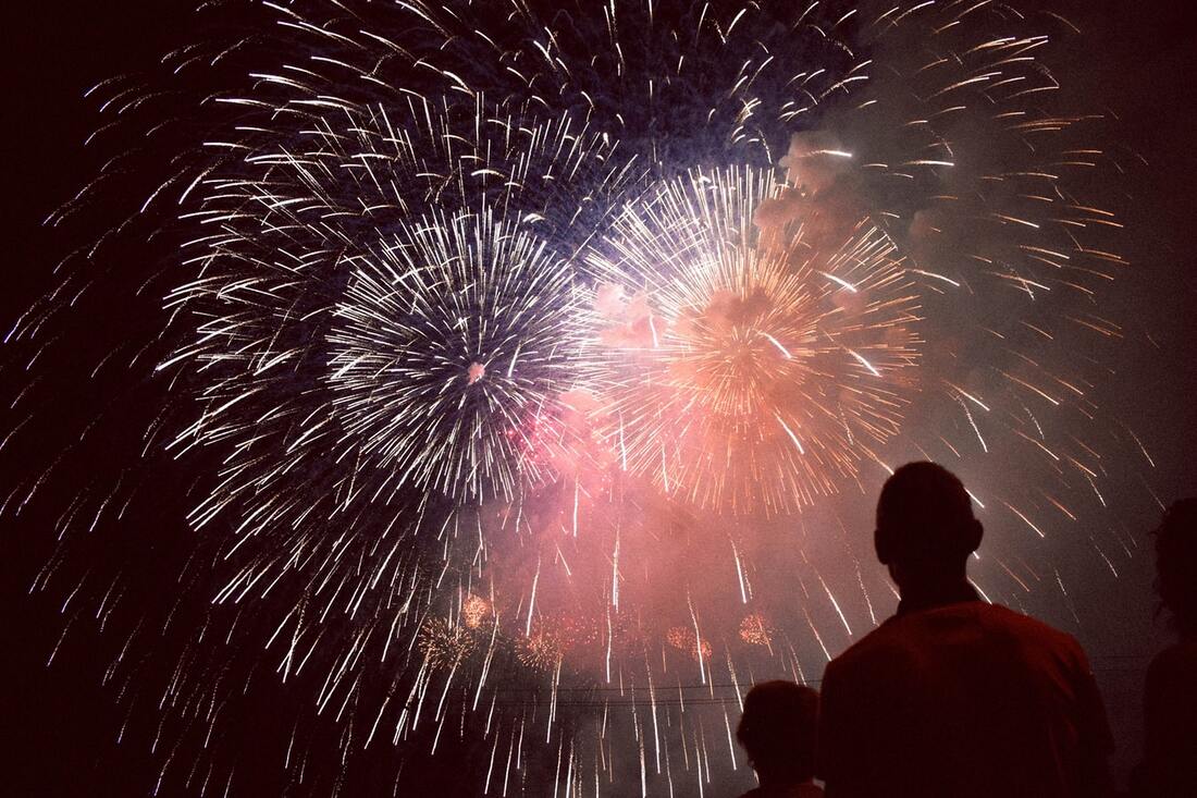 silhouette of people standing and looking up at bursts of fireworks display at night