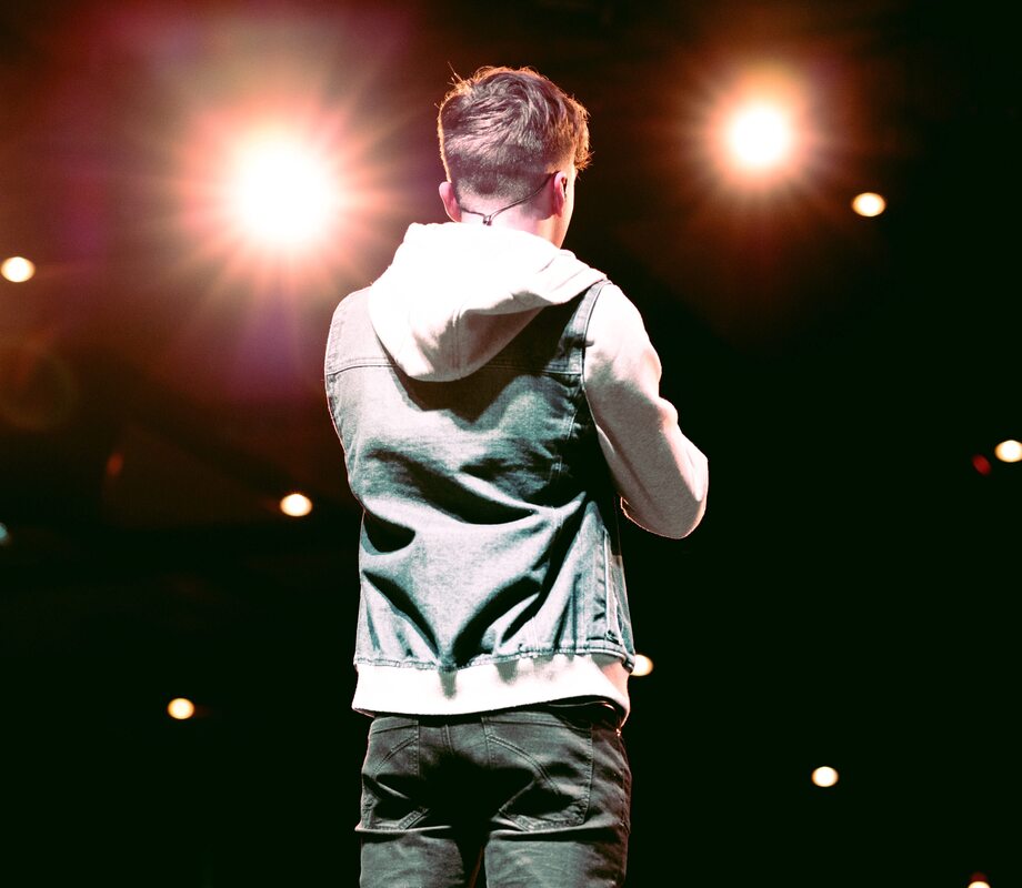 singer with hearing loss wears hoodie and jeans on bright lit stage