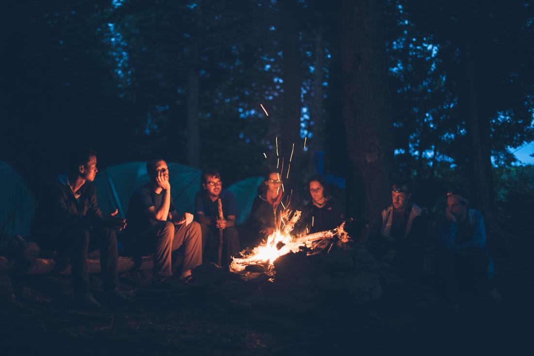 group of friends gathered around campfire listen to crackling noises and talking
