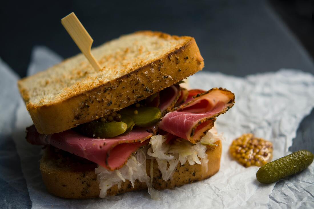 A pastrami sandwich with mustard, sauerkraut, and pickles has a toothpick inserted through the center.