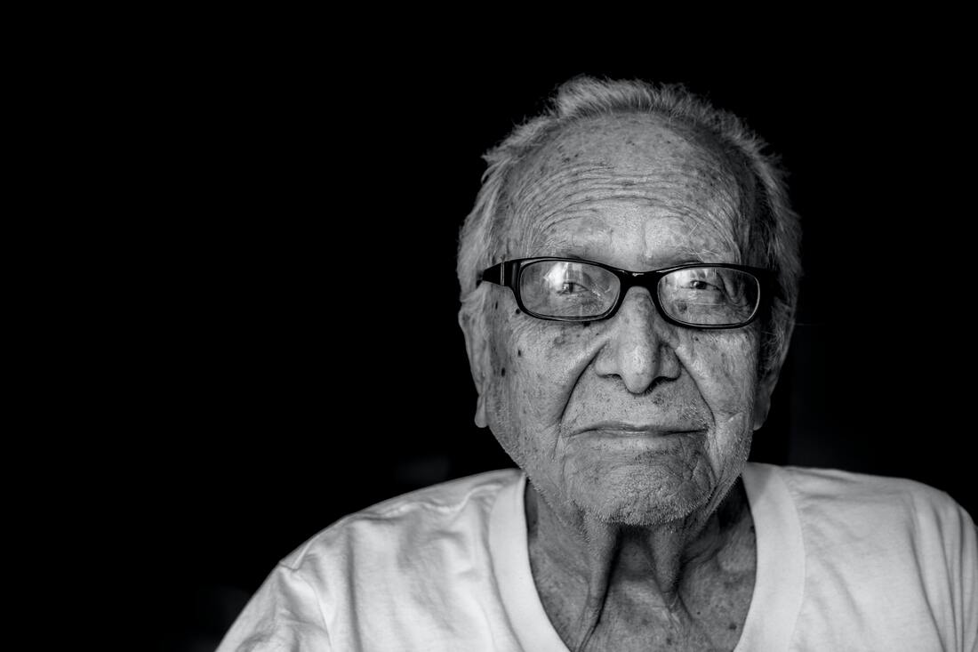 old_man_with_black_framed_glasses_white_shirt_black_background_uses_hearing_aids_to_treat_hearing_loss_and_dementia 