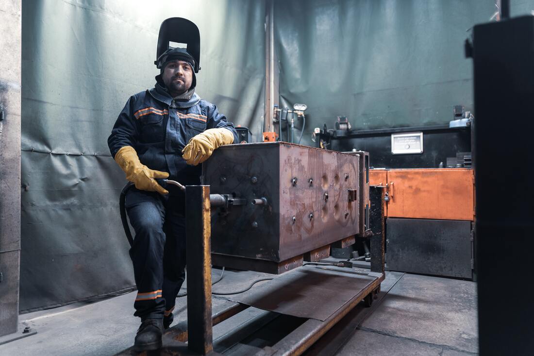man_with_hearing_loss_wears_welding_suit_and_mask_stands_next_to_machine
