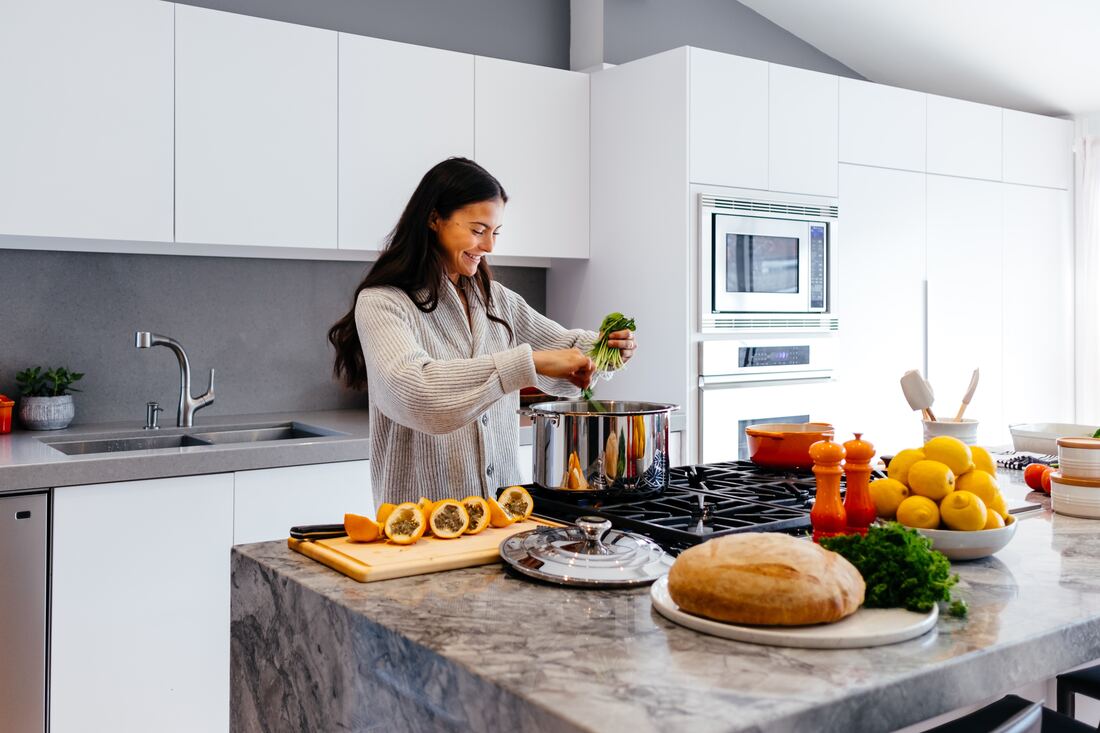 young woman cooks vegetables at stovetop in white and grey kitchen