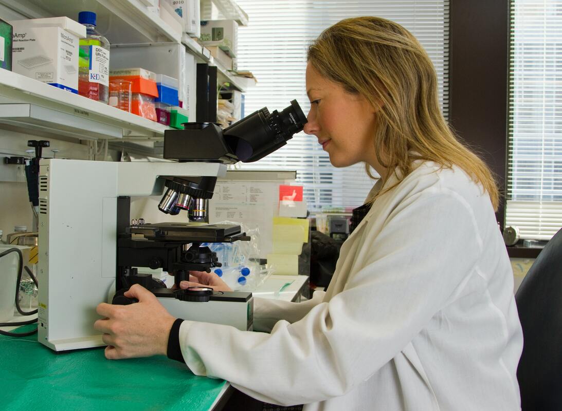 scientist-in-white-coat-looks-through-microscope-in-lab