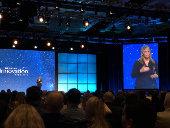 woman speaks about technology on stage at hearing aid convention