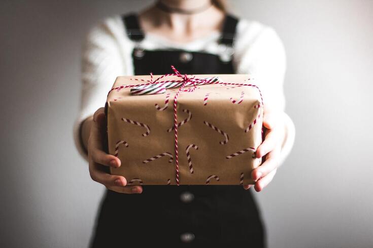 woman wearing overalls holds brown paper with candy canes gift box containing hearing aids