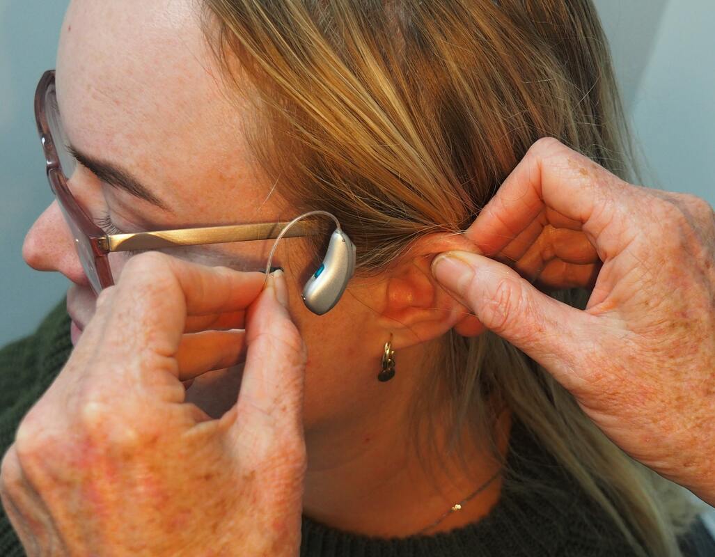 woman with eye glasses and earings receives behind the ear hearing aid fitting in strasburg
