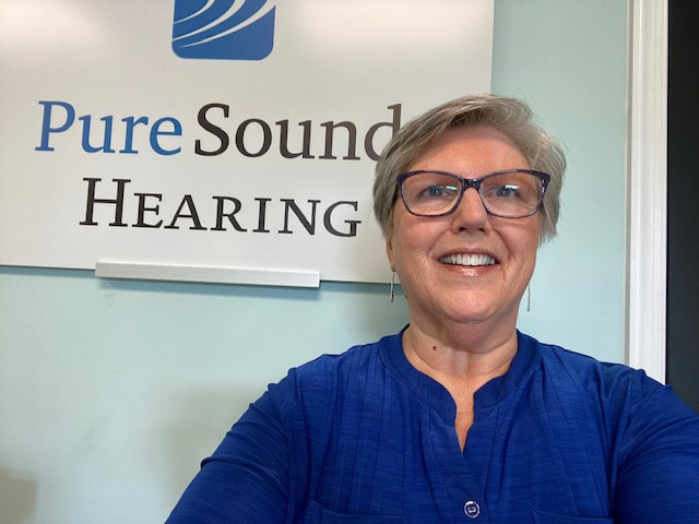 woman with eyeglasses and blue blouse in front of pure sound hearing sign