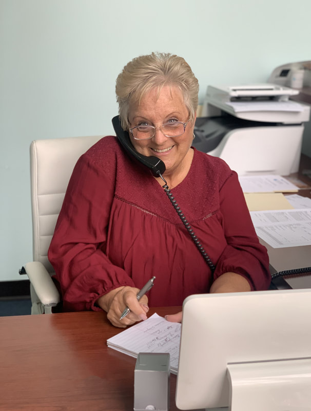 woman with glasses and red blouse smiles and answers phone in elizabethtown hearing aid office