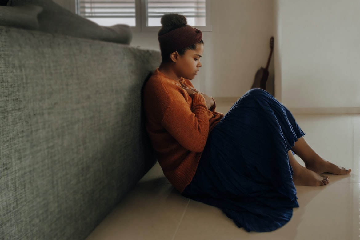 woman with orange sweater and blue skirt has hearing loss and anxiety while sitting on living room floor against couch